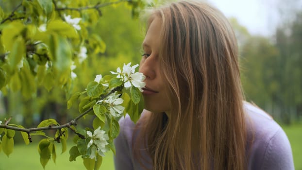 Close up portrait of happy woman near apple tree in blossom. She is smelling flowers. Beauty in nature. Real people