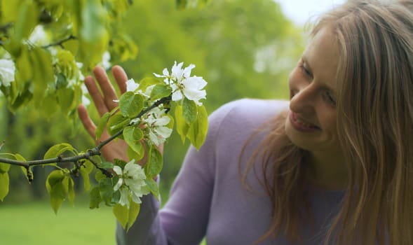 Close up portrait of happy woman near apple tree in blossom. She is watching flowers. Beauty in nature. Real people