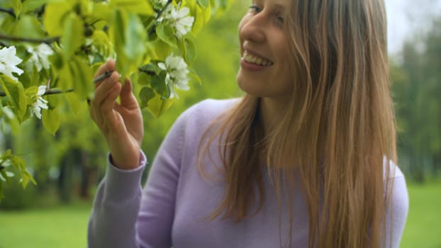 Close up portrait of happy woman near apple tree in blossom. She is watching flowers. Beauty in nature. Real people