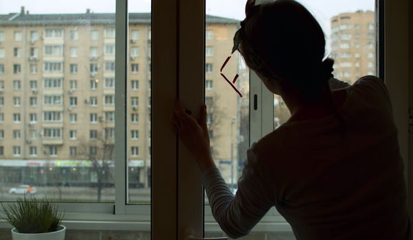 Silhouette of a young woman writing on window glass using lipstick. Rear view