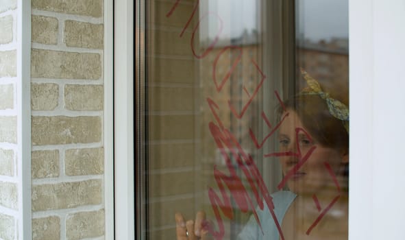 Young beautiful woman writing word "Freedom" on the window glass using lipstick. The end of quarantine. View through a glass outside. Buildings reflected in the window.