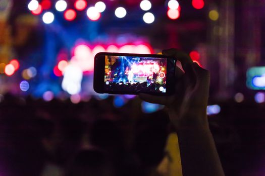 Hand with a smartphone records live music festival, Taking photo of concert stage, live concert, music festival, happy youth, luxury party, landscape exterior