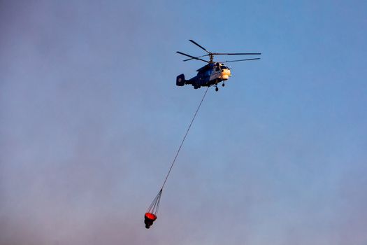 Chalkidiki, Greece - Sept 22, 2017: Firefighting helicopter with a bucket of water as he tries to extinguish a fire in a pine forest in Kassandra, Halkidiki