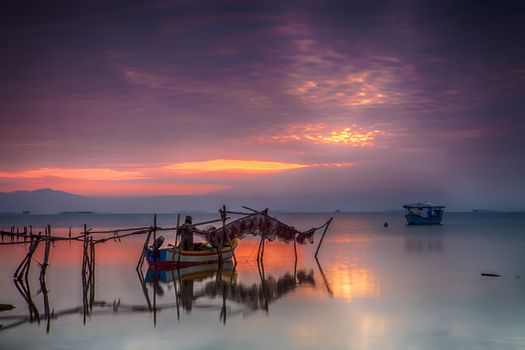 View of a beautiful sky reflecting on the ocean and a fisherman on his boat hanging fishing nets.