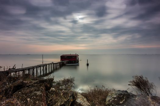 Long exposure of magic sunrise over the ocean with a hut in the middle and a wooden bridge. Photographed using ND filter