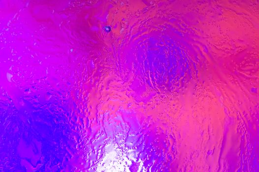 The hue purple abstract composition of oil drops in water with soft focus effect and black insect swimming in oil.