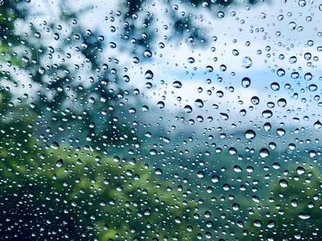Beautiful closeup & focused view of raindrops on the car window with the blurred nature forest green trees in the background