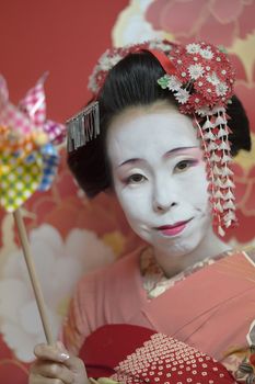 Maiko in kimono holding a colorful pipe wind turbine in the hand.