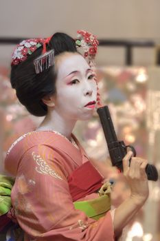 Pretty young Geisha maiko girl in kimono holding a plastic gun in her hand.