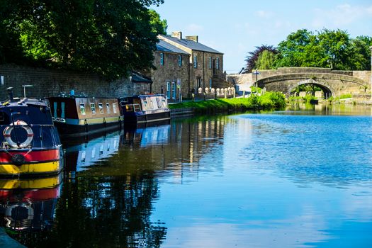 View down Lancaster canal towards a row of narrowboats with a bridge in the background