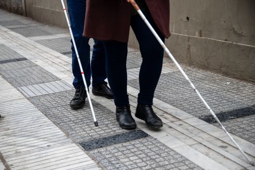 blind man and woman walking on the street using a white walking stick