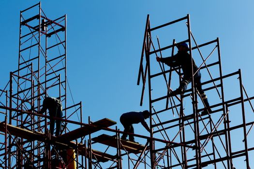 silhouette of construction workers against sky on scaffolding with ladder on building site