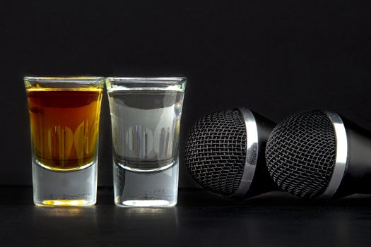 Shoot Glasses with liquor and two karaoke microphones on a black background