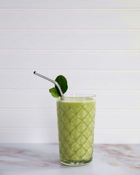 Green milkshake with straw and leaf on a marble table