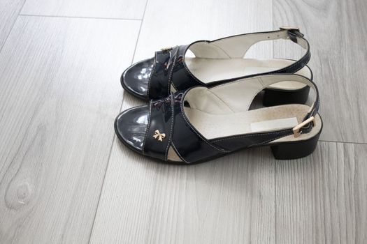 Women's patent leather sandals with a metal bow on small heels. Back strap in sandals, open heel. Sandals stand on a gray parquet.