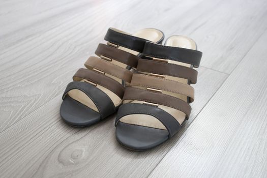Women's shoes with small heels with straps stand on a gray parquet. The straps are fastened with metal parts