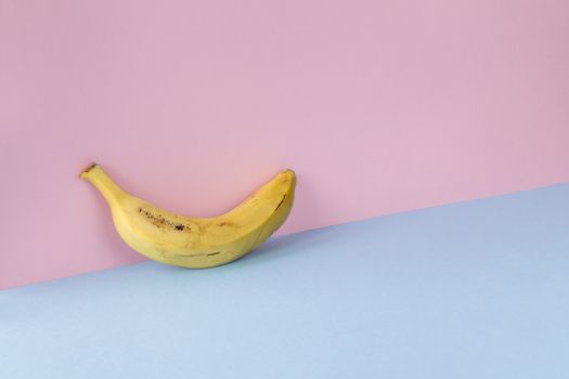 Minimalist image of a banana on a light blue and pink background. Copy space available.