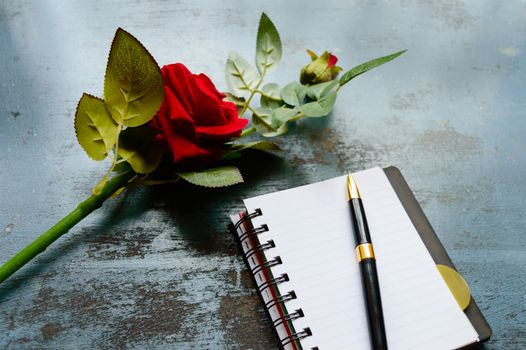 Blank Page Notebook, pen and a Beautiful red rose on rustic metal floor background with copy space. Love letter Writing Proposal or propose concept for valentines day wedding and holidays. Top view.