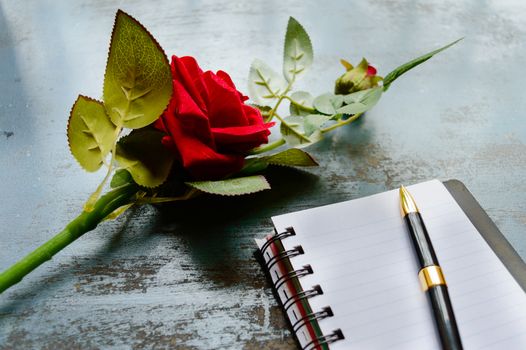 Blank Page Notebook, pen and a Beautiful red rose on rustic metal floor background with copy space. Love letter Writing Proposal or propose concept for valentines day wedding and holidays. Top view.