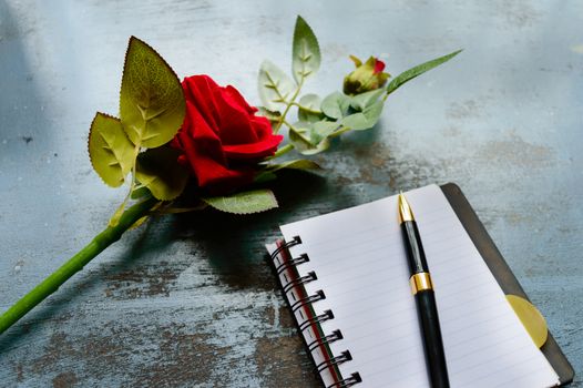 Blank Page Notebook, pen and a Beautiful red rose on rustic metal floor background with copy space. Love letter Writing Proposal or propose concept for valentines day wedding and holidays. Top view.