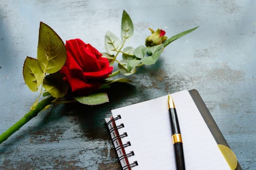 Blank Page Notebook, pen and a Beautiful red rose on rustic metal floor background with copy space. Love letter Writing Proposal or propose concept for valentines day wedding and holidays. Top view.