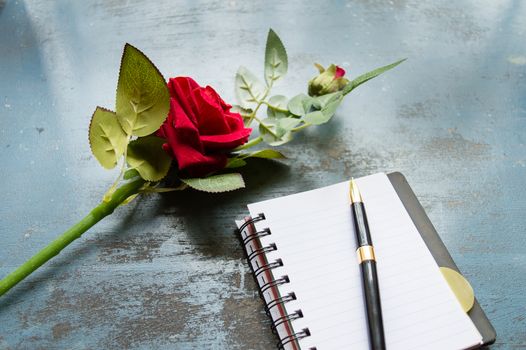 Blank Page Notebook, pen and a Beautiful red rose on rustic metal floor background with copy space. Love letter Writing Proposal or propose concept for valentines day wedding and holidays. Top view.