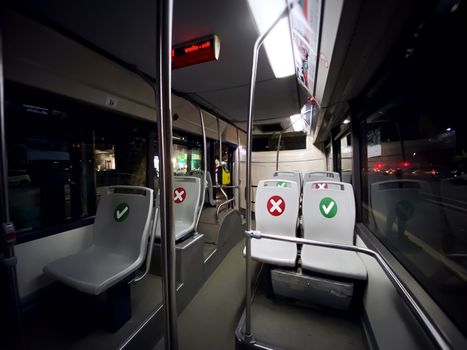interior of a public transport bus with empty seats with the indication of where is possible to sit during the coronavirus pandemic. Transport and urban mobility. Wide angle shot