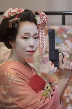 Maiko in kimono holding a plastic gun in her hand.