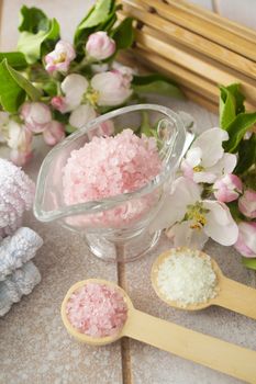 Spa or wellness setting. Pink sea salt, towels and apple blossom on shabby wooden table.
