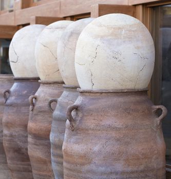 Large clay brown pots are covered with stone eggs and stand in a row for sale