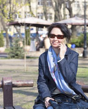 Portrait of a young, beautiful woman sitting on a bench in a spring park and smiling talking on the phone