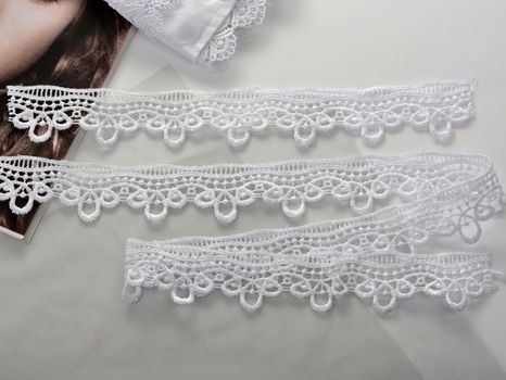 Tapes of white gentle guipure, beauty lace fabric on light background. Elastic material. Using for Atelier and needlework store.