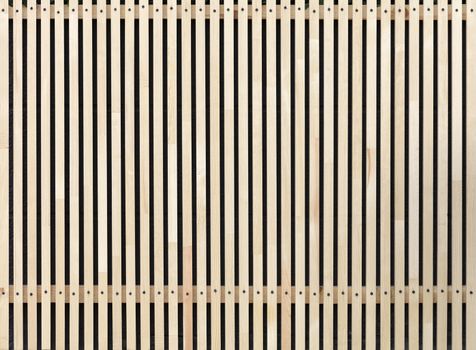 A new fence made of smooth wooden slats fixed with metal screws on transverse wooden bars against the backdrop of a black stone wall