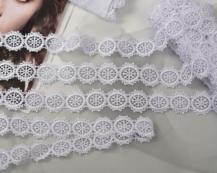 Tapes of white gentle guipure, beauty lace fabric on light background. Elastic material. Using for Atelier and needlework store.