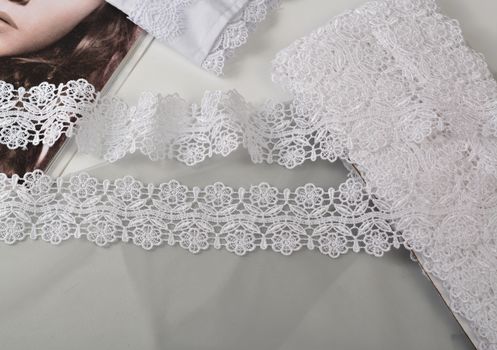 Tapes of white gentle guipure, beauty lace fabric on light background. Elastic material. Using for Atelier and needlework store.