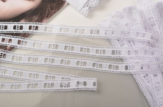 Tapes of white gentle guipure, beauty lace fabric on light background. Elastic material. Using for Atelier and needlework store.