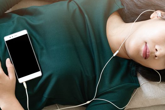 Over head view of beautiful young woman laying down on sofa using smartphone to listen the music