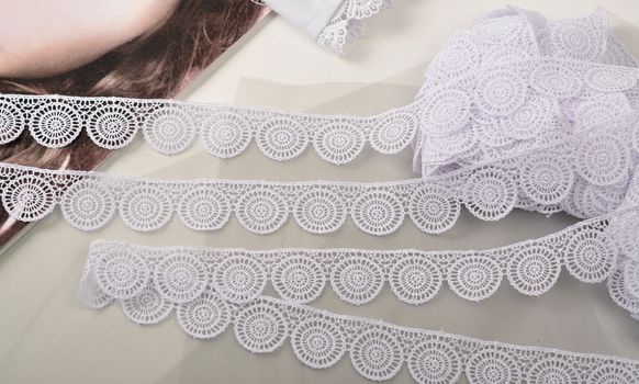 Tapes of white gentle guipure, beauty lace fabric on light background. Elastic material. Using for Atelier and needlework store.