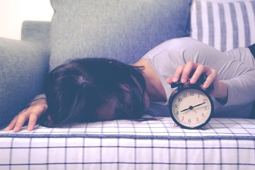 Lazy women is laying down on the sofa after the clock alarm, late wakeup lifestyle concept