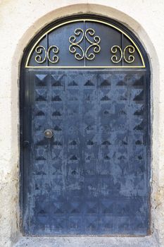 An old iron door with a faded stone arch, a metallic gold frame and a wrought iron lock