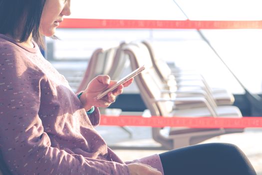 young women texting on mobile phone waiting for flying at airport window