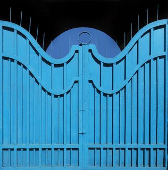 Old metal gate-fence with original structure painted in bright blue paint on the background of the archway