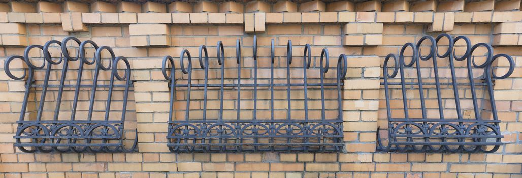 The fence of brickwork is decorated with a forged curly iron grating