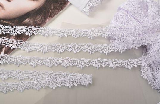 Tapes of white gentle guipure, beauty lace fabric on light background. Elastic material. Using for Atelier and needlework store.