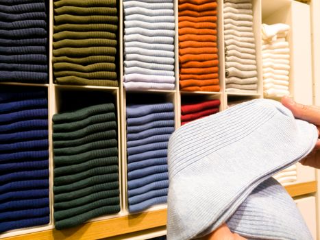 women hand pick the light blue sock from socks stack on shelves for sale in clothing store