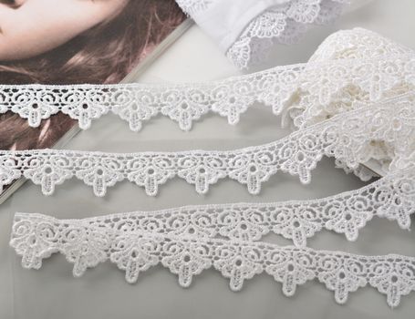 Tapes of white gentle guipure, beauty lace fabric on light background. Elastic material. Using for Atelier and needlework store.