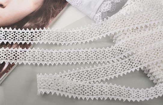 Tapes of white gentle guipure, beauty lace fabric on light background. Elastic material. Using for Atelier and needlework store.