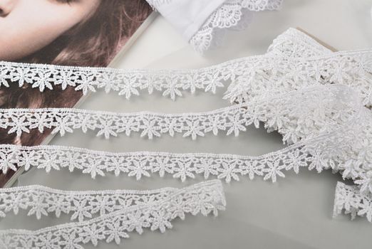 Tapes of white gentle guipure, beauty lace fabric on light background. Elastic material. Using for Atelier and needlework store.