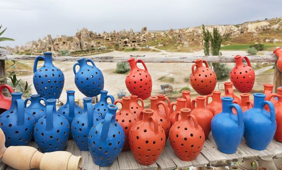 Blue and red clay pots of desires stand on a wooden coarse table made of weathered planks against the backdrop of the caves of Cappadocia.