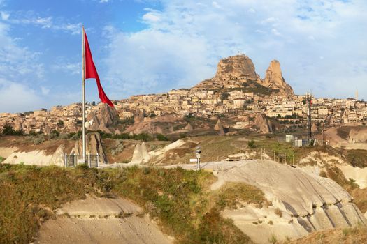 Great national flag of Turkey against the background of the city-cave Uchhisar and the blue sky. Cappadocia, central Turkey.